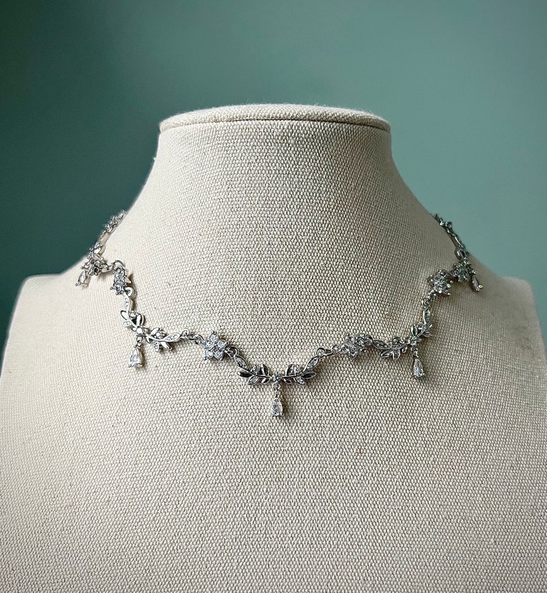 May include: A silver necklace with a delicate floral design and dangling crystal accents.