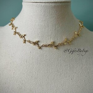 May include: A gold necklace with a delicate vine design and small clear stones. The necklace is on a white mannequin bust.