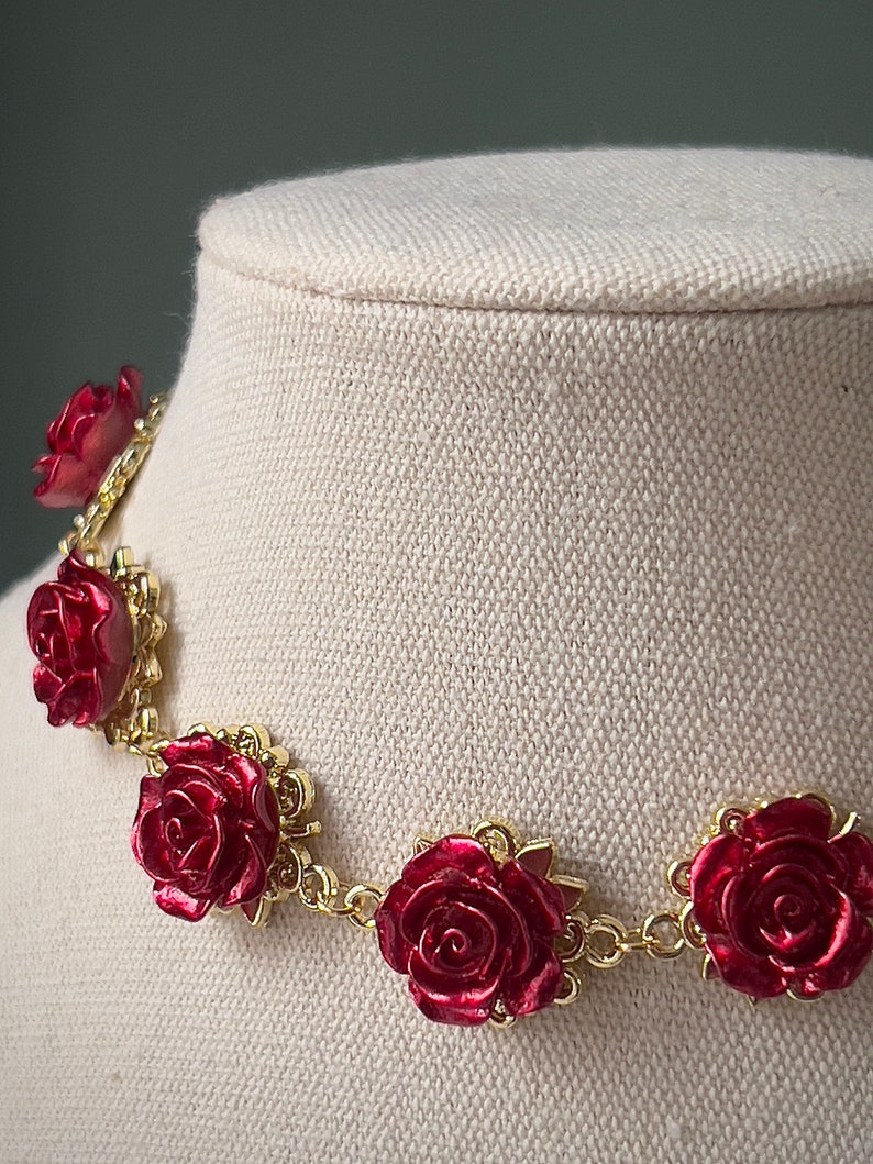 May include: A gold chain necklace with red rose accents. The roses are 3D and have a glossy finish.