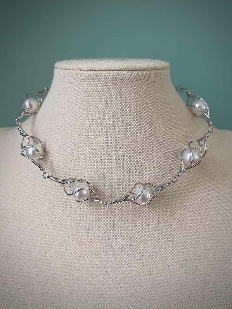May include: A silver wire necklace with white pearls set in a twisted wire design.