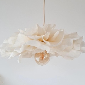Op de afbeelding: Een crèmekleurige papieren bloem hanglamp. De lamp heeft een groot, gelaagd bloemendesign met een zichtbare gloeilamp. De lamp hangt aan een beige snoer tegen een witte achtergrond. De lamp is een decoratief item voor in huis.