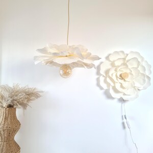 May include: A white, flower-shaped pendant light fitting with a visible lightbulb hangs from the ceiling. A matching flower-shaped wall decoration is mounted on the wall. A woven vase with dried plants is on the left.
