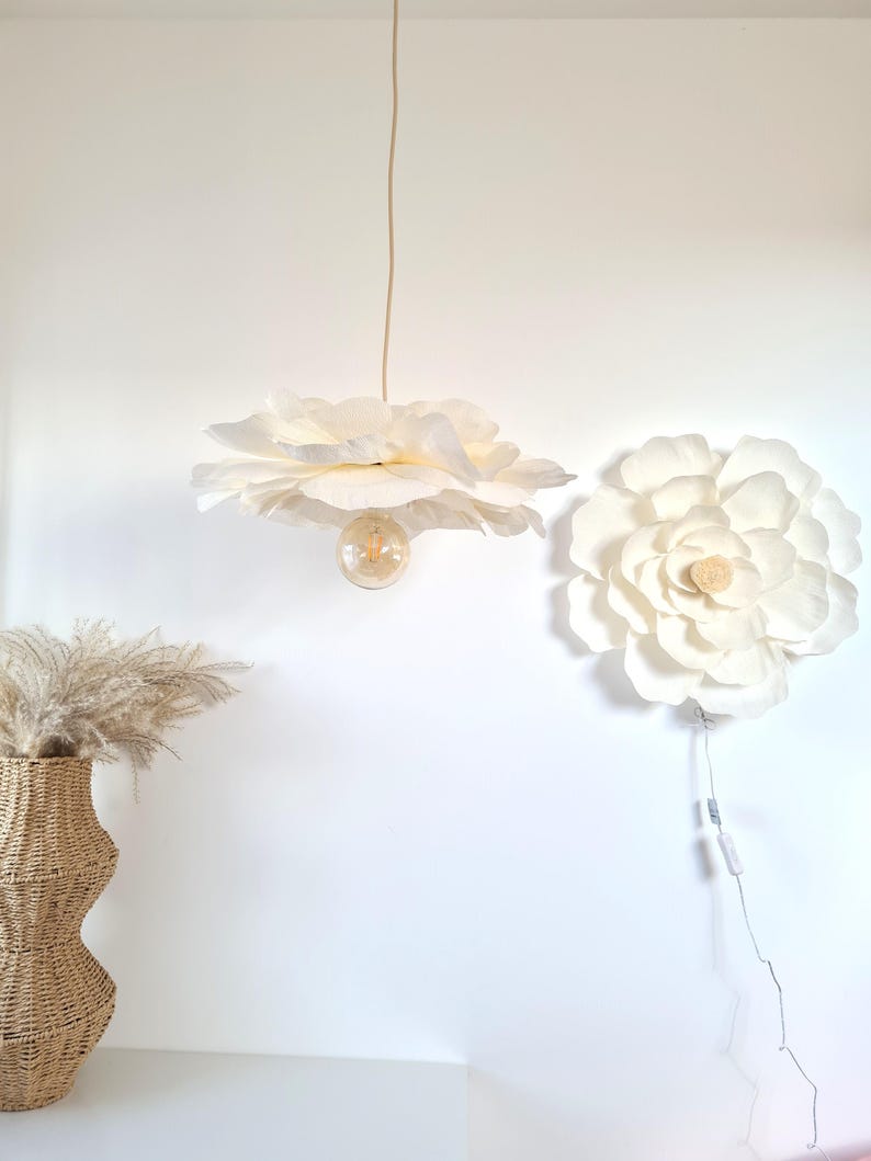 May include: A white, flower-shaped pendant light fitting with a visible lightbulb hangs from the ceiling. A matching flower-shaped wall decoration is mounted on the wall. A woven vase with dried plants is on the left.