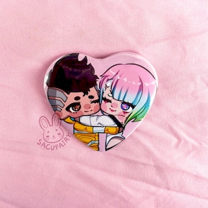 May include: Heart-shaped button featuring two anime-style characters embracing. One character has dark hair and the other has pink and blue hair. The button is set against a pink background.