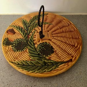 Puede incluir: Plato de cerámica redondo para servir con un diseño de tejido de cesta en tonos marrones y amarillos. Presenta un diseño botánico verde y marrón y un asa negra. Una pieza decorativa para servir alimentos, de unos 25 cm de diámetro.