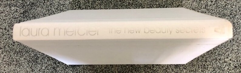 May include: White book with the title "laura mercier the new beauty secrets" printed on the spine.