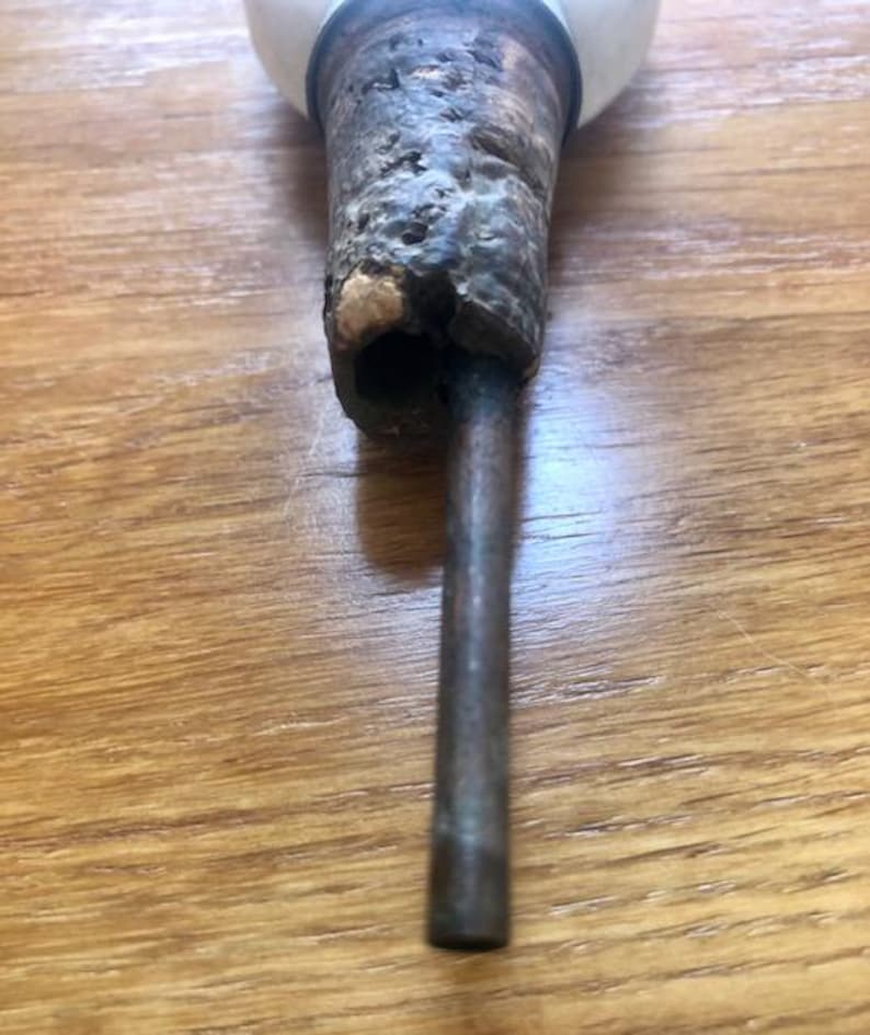 K&ouml;nnte beinhalten: Nahaufnahme eines Vintage-Flaschenverschlusses. Der Verschluss hat einen verwitterten, strukturierten Holzgriff mit dunklem, gealtertem Aussehen. Eine Metallstange erstreckt sich vom Griff, und eine wei&szlig;e, abgerundete Oberseite ist sichtbar.