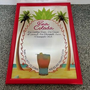 May include: A framed sign with a red border features a "Pina Colada" recipe. The design includes palm trees, a cocktail illustration, and the recipe: 2 oz golden rum, 2 oz cream of coconut, 4 oz pineapple juice, and 1 pineapple stick.