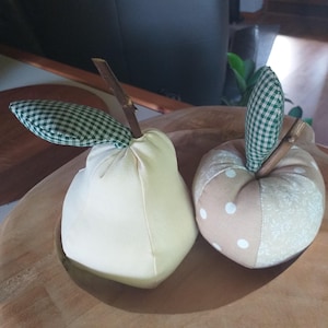 Könnte beinhalten: Zwei Stoff-Fruchtdekorationen, eine Birne und ein Apfel, in einer Holzschale. Die Birne ist weiß mit einem grünen Gingham-Blatt und Stiel. Der Apfel ist braun mit weißen Punkten und einem grünen Gingham-Blatt und Stiel.