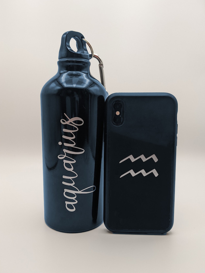 May include: A glossy black metal water bottle with a silver carabiner and the word "aquarius" written in a cursive script, positioned next to a black smartphone case featuring a silver Aquarius zodiac symbol consisting of two wavy lines.