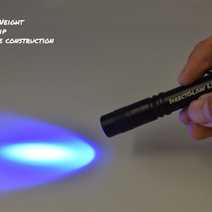 May include: A black flashlight with the text "DIRECTGLOW LLC" on the side, emitting a bright blue light beam. The flashlight is being held in a hand.