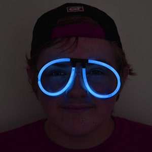 May include: A person wearing a black baseball cap with a white logo and blue glow-in-the-dark glasses.