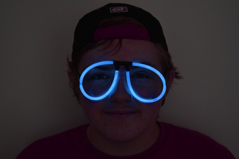 May include: A person wearing a black baseball cap with a white logo and blue glow-in-the-dark glasses.