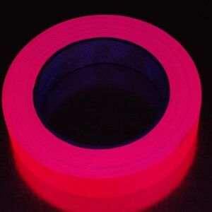 K&ouml;nnte beinhalten: Eine Rolle leuchtend pinkfarbenes fluoreszierendes Klebeband. Das Band ist um einen schwarzen Kern gewickelt.