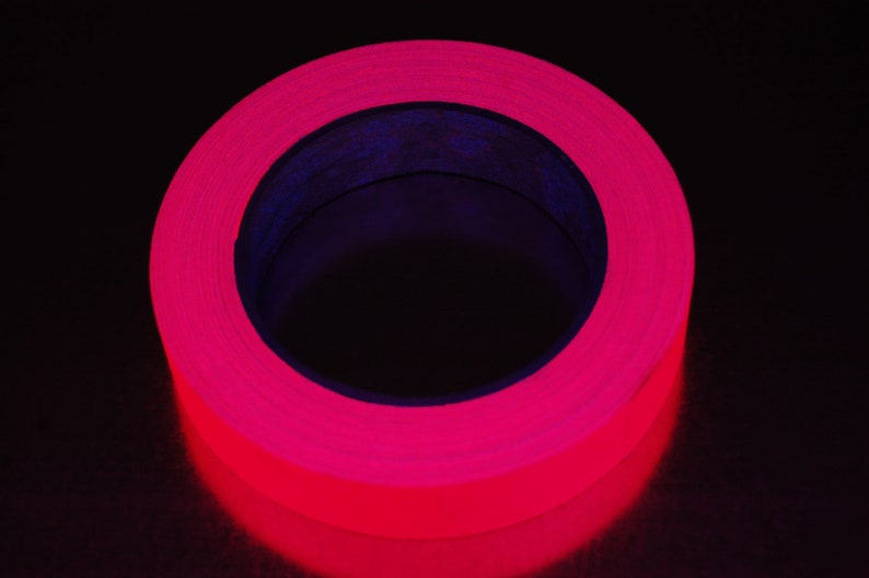 K&ouml;nnte beinhalten: Eine Rolle leuchtend pinkfarbenes fluoreszierendes Klebeband. Das Band ist um einen schwarzen Kern gewickelt.