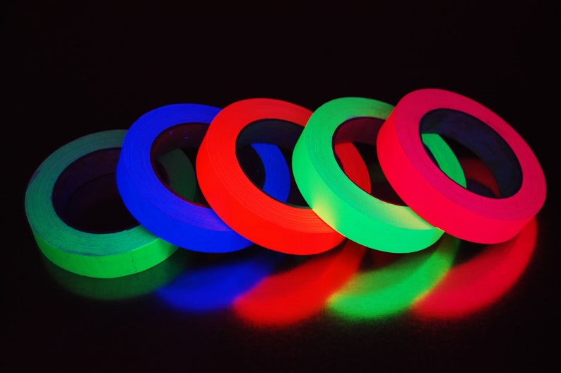 K&ouml;nnte beinhalten: F&uuml;nf Rollen Neon-Klebeband in den Farben Gr&uuml;n, Blau, Rot, Gr&uuml;n und Pink sind in einem Halbkreis auf einer schwarzen Oberfl&auml;che angeordnet.