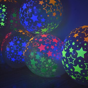 May include: A group of colorful balloons with star patterns. The balloons are translucent and glow in the dark. The colors of the stars are green, blue, red, and orange.