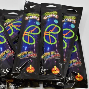 May include: A pile of black plastic bags with glow in the dark glasses inside. The bags have a glow in the dark design and say "Glow in the Dark" and "Glow Glasses".