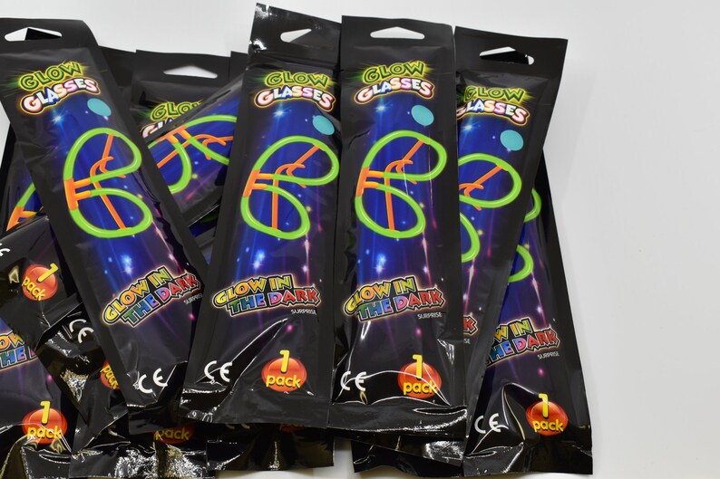 May include: A pile of black plastic bags with glow in the dark glasses inside. The bags have a glow in the dark design and say "Glow in the Dark" and "Glow Glasses".