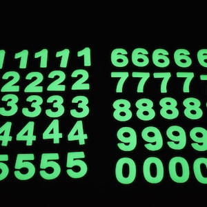 May include: A set of glow-in-the-dark numbers, from 0 to 9, arranged in rows. Each number is repeated five times, creating a grid pattern. The numbers are a bright green color and are visible against a black background.