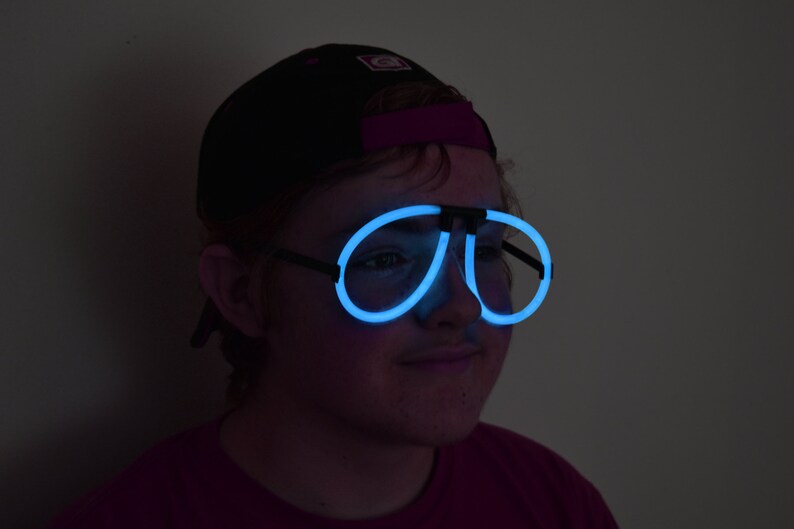 May include: A person wearing a black baseball cap and blue glow-in-the-dark glasses.