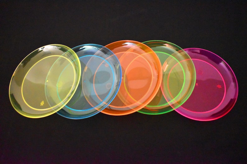 May include: Five plastic plates in a rainbow of colors: yellow, blue, orange, green, and pink. The plates are translucent and have a slight sheen.