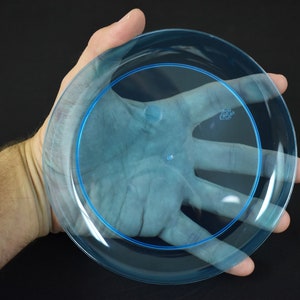 May include: A clear blue plastic plate with a slightly raised rim. The plate is being held in a hand.