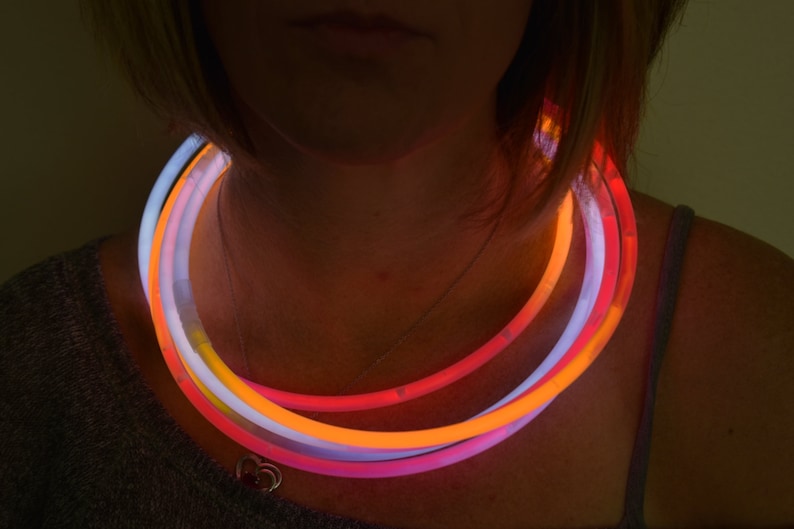 May include: A set of three circular glow necklaces in vibrant neon colors, including bright orange, pink, and white. These flexible, tubular light-up accessories are worn around the neck, emitting a steady, luminous glow that illuminates the surrounding area.