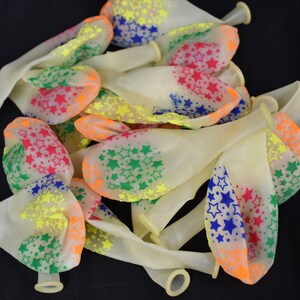 May include: A bunch of white latex balloons with a multi-colored star pattern. The stars are in shades of red, orange, yellow, green, and blue.