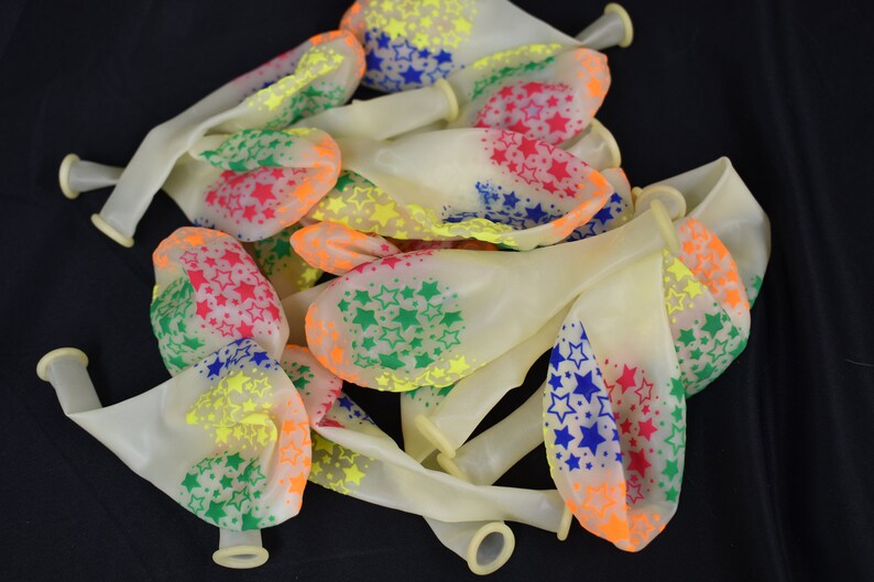 May include: A bunch of white latex balloons with a multi-colored star pattern. The stars are in shades of red, orange, yellow, green, and blue.