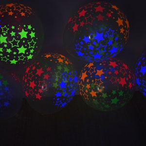 May include: A group of six black balloons with neon star patterns. The balloons are filled with helium and are floating in the air. The stars are in different colors, including green, blue, orange, and red.