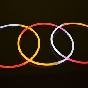 May include: Three circular glow necklaces arranged in an overlapping pattern. Each necklace features a translucent plastic tube that emits light in distinct colors, including white, orange, and red, with small white plastic connectors at the ends.