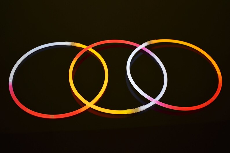 May include: Three circular glow necklaces arranged in an overlapping pattern. Each necklace features a translucent plastic tube that emits light in distinct colors, including white, orange, and red, with small white plastic connectors at the ends.