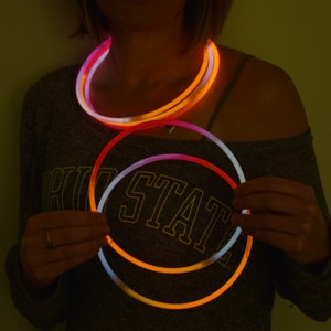 May include: A set of flexible, circular glow sticks that emit a bright, neon orange and white light. The sticks are arranged in overlapping loops, creating a vibrant, luminous effect against the dark, low-light environment of the scene.
