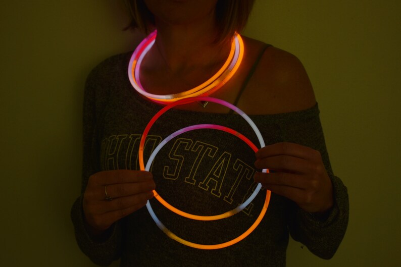May include: A set of flexible, circular glow sticks that emit a bright, neon orange and white light. The sticks are arranged in overlapping loops, creating a vibrant, luminous effect against the dark, low-light environment of the scene.