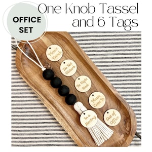 May include: A wooden tray with a white tassel and six wooden tags with different phrases. The tags say "Please Knock", "Do Not Disturb", "Be Right Back", "Please Come In", "In a Meeting", and "Out of Office".