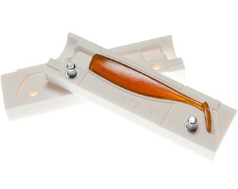 May include: A white plastic mold for making fishing lures. The mold is open and a 3-inch orange lure is inside. The mold is labeled "S13 3".
