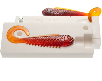 May include: Two white plastic molds for making fishing lures. The molds are open and show two red and orange fish-shaped lures with glitter. The molds are labeled "G4 2.7".