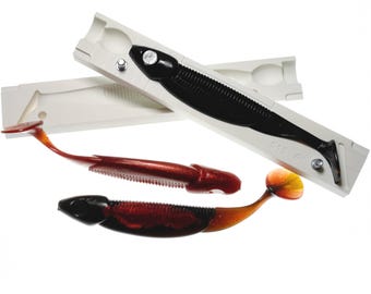 May include: A black and brown soft plastic fishing lure with a white mold. The lure is 6 inches long and has a detailed design. The mold is white and has a cavity for the lure. The image is on a white background.
