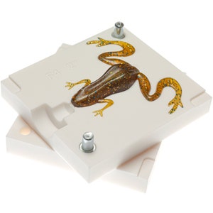 May include: A white plastic mold for making a 2-inch frog lure. The mold is open and a brown and gold frog lure is inside. The mold has the text "F4 2" on it.