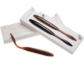 May include: A white plastic mold for making two 4.25 inch long fishing lures. The mold is open and two brown lures are partially inserted. One lure is fully removed and lying on a white surface.