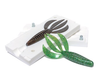 May include: Two plastic molds for making fishing lures. One mold is brown and the other is green. The molds are open and show the finished lures inside.