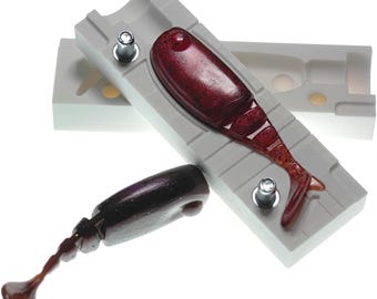 May include: A two-piece plastic mold for making fishing lures. The mold is open and a red and brown lure is in the mold. A finished lure is also shown.
