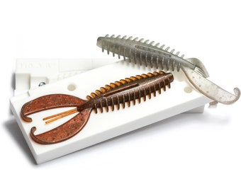May include: Two brown and grey plastic fishing lures in a white plastic mould. The lures have a segmented body and a forked tail.