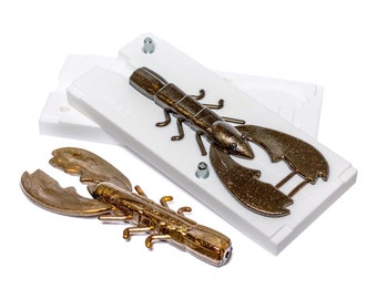 May include: A white plastic mold for making a brown and gold lobster-shaped fishing lure. A finished lure is shown next to the mold.