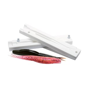 May include: Two white plastic moulds for making fishing lures. The moulds are open and show the inside of the mould. Two finished lures are shown in the foreground, one black and one pink.