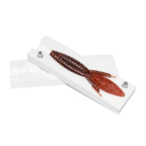 May include: A white plastic mold for making fishing lures. The mold is open and a brown and red lure is inside.