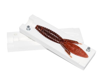 May include: A white plastic mold for making fishing lures. The mold is open and a brown and red lure is inside.