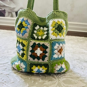 K&ouml;nnte beinhalten: Eine gr&uuml;ne geh&auml;kelte Tragetasche mit Patchwork-Muster aus bunten Quadraten. Die Quadrate sind in den Farben Gr&uuml;n, Gelb, Blau, Wei&szlig; und Braun gehalten.