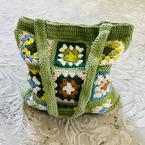 K&ouml;nnte beinhalten: Eine gr&uuml;ne geh&auml;kelte Tragetasche mit bunten quadratischen Mustern. Die Tasche hat zwei Henkel und ist mit einem Granny-Square-Stich gearbeitet.